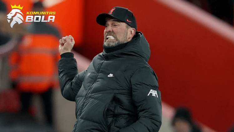Jürgen Klopp mengenakan jaket hitam dan topi Liverpool sambil melakukan selebrasi di pinggir lapangan saat pertandingan berlangsung.